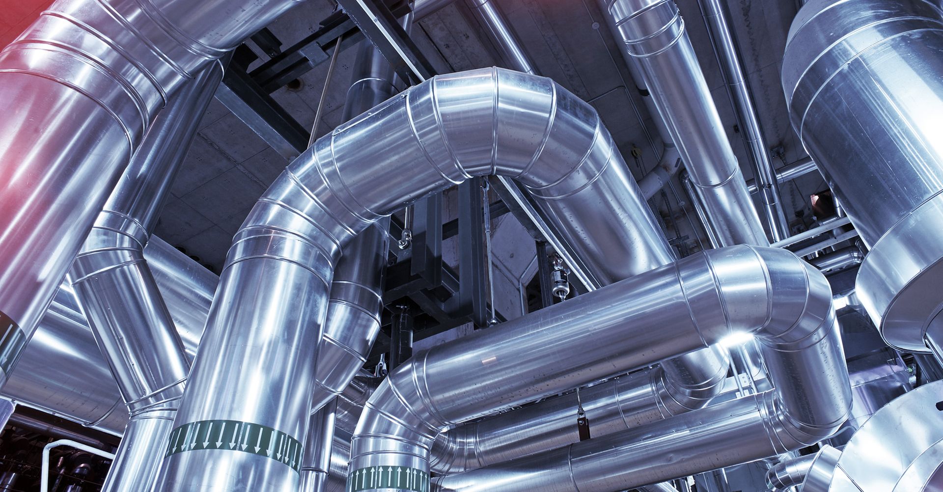 Ein Blick nach oben in einer Industrieanlage, die ein dichtes Netzwerk aus großen, gebogenen Rohren und Ventilen zeigt.